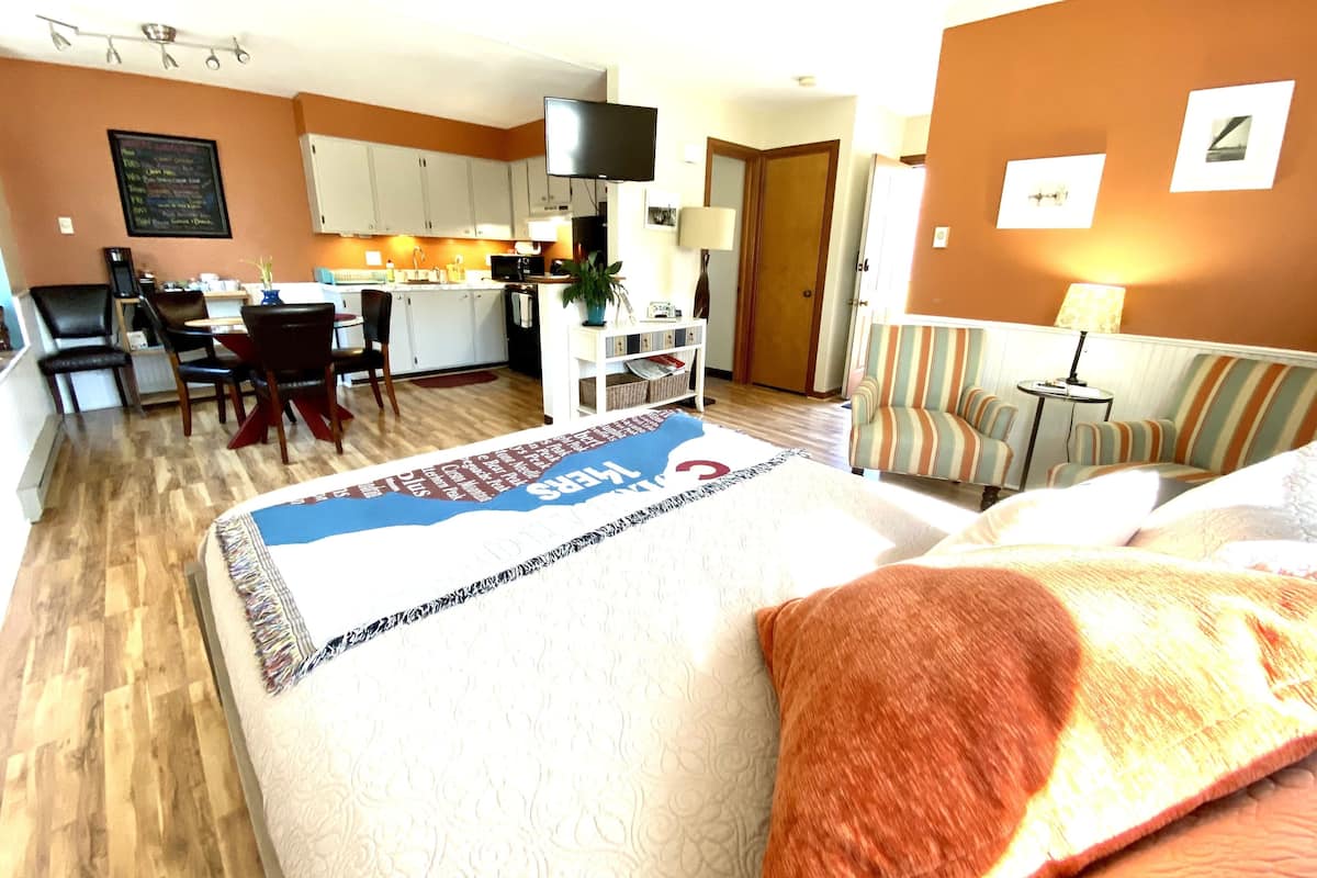 Quarto de hotel com cama, sofá, área de refeições e cozinha.