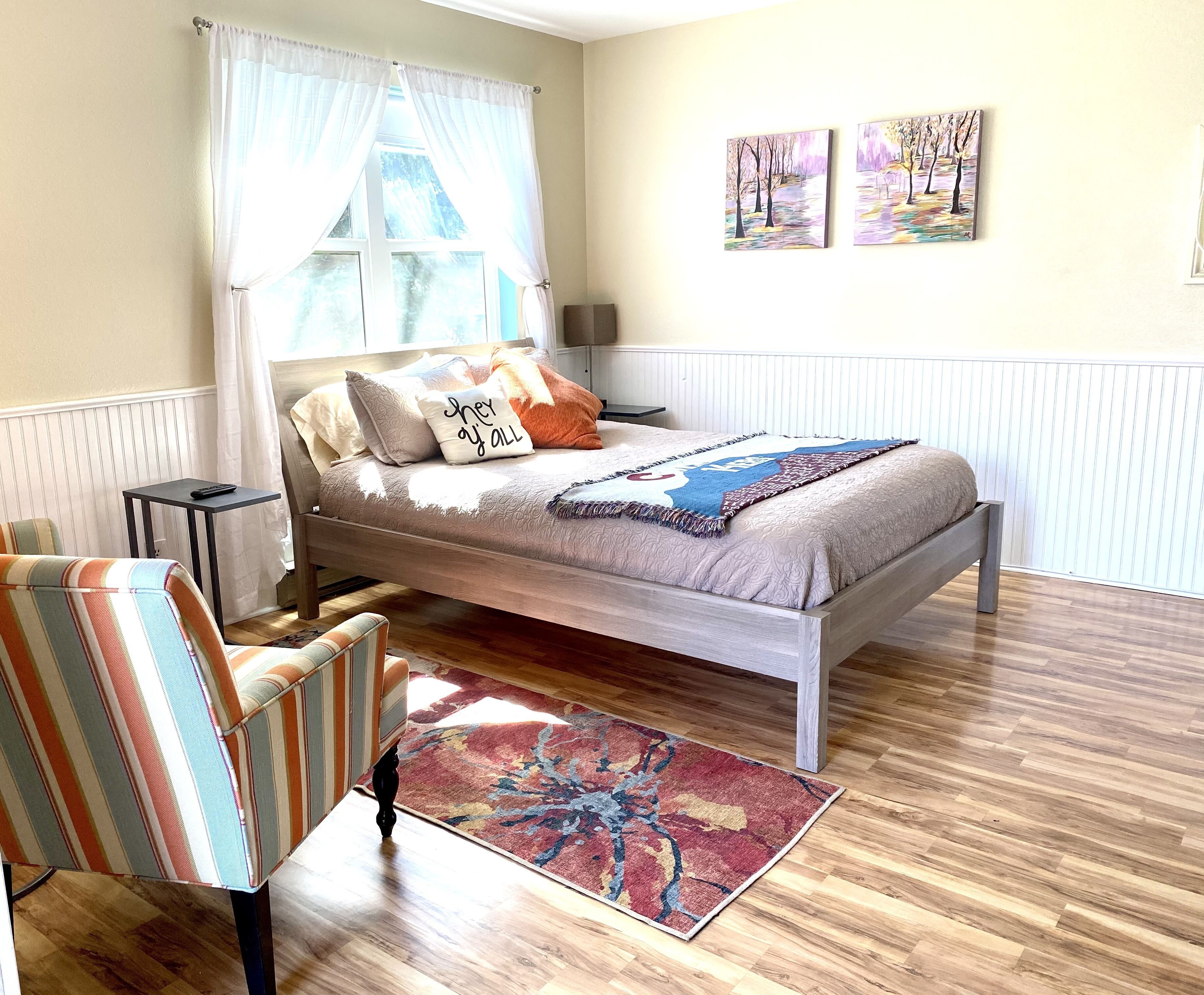 Ein Schlafzimmer mit einem Bett, einem gestreiften Sessel, einem kleinen Tisch und einem Teppich.