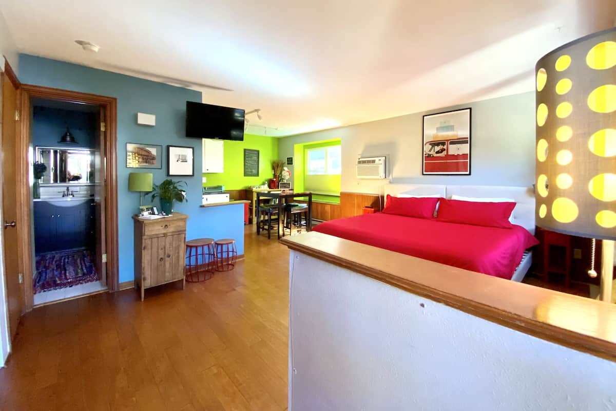 Quarto de hotel com cama, escrivaninha, cadeira, televisão e banheiro.