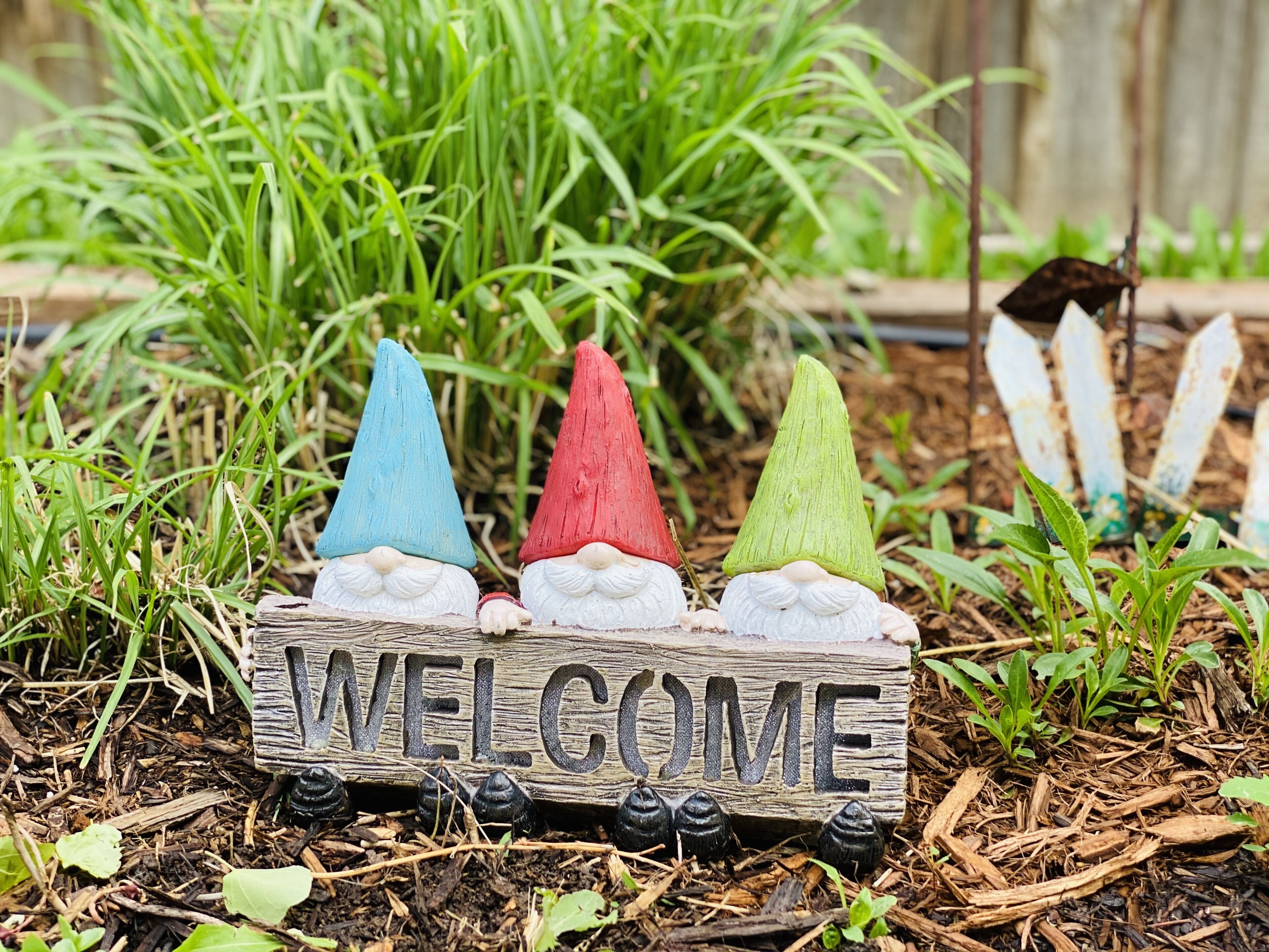 A wooden sign with the word "WELCOME" and three gnome figures in blue, red, and green.