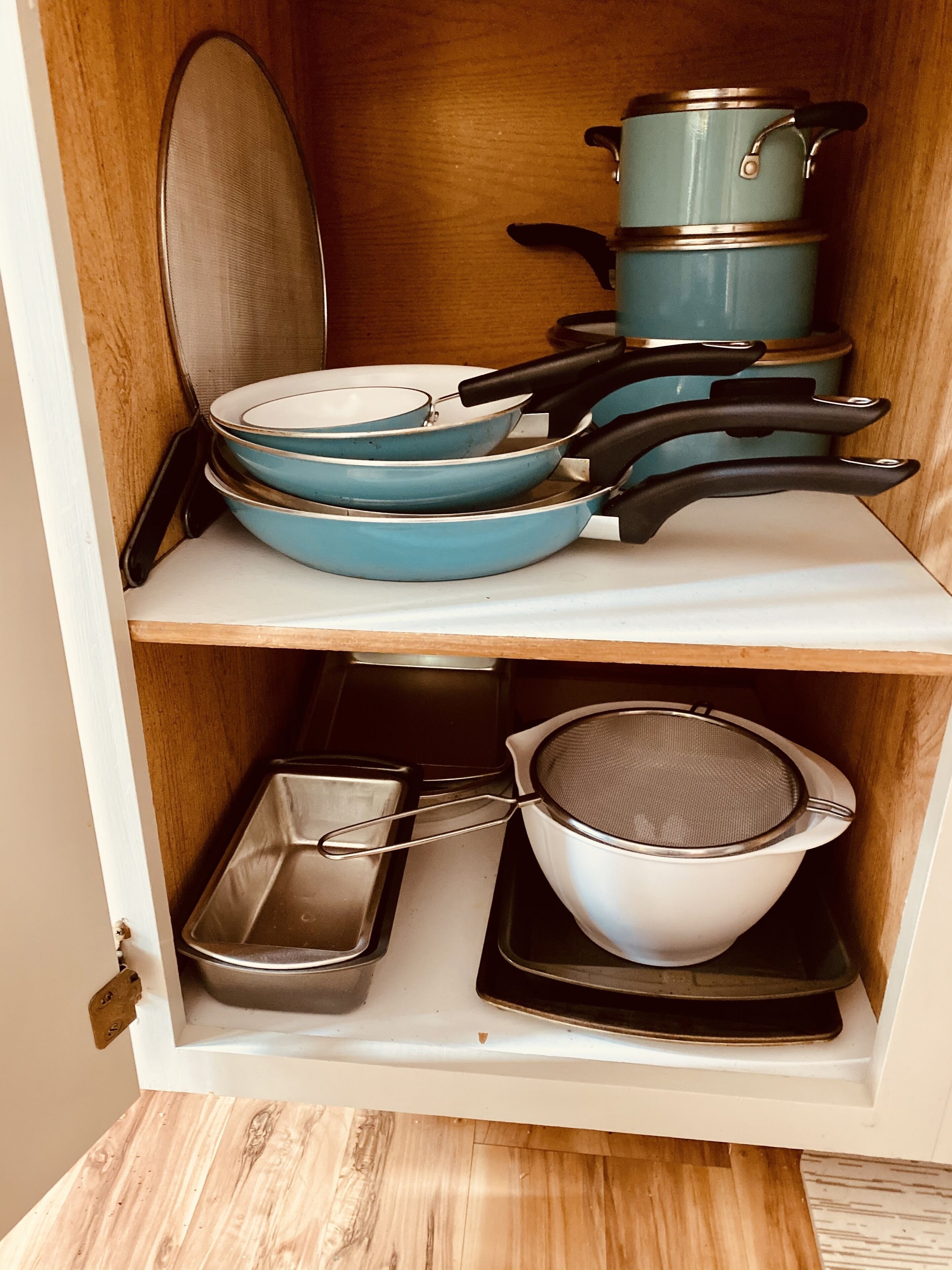 Un armario de cocina con utensilios de cocina, incluyendo ollas, sartenes y un colador.