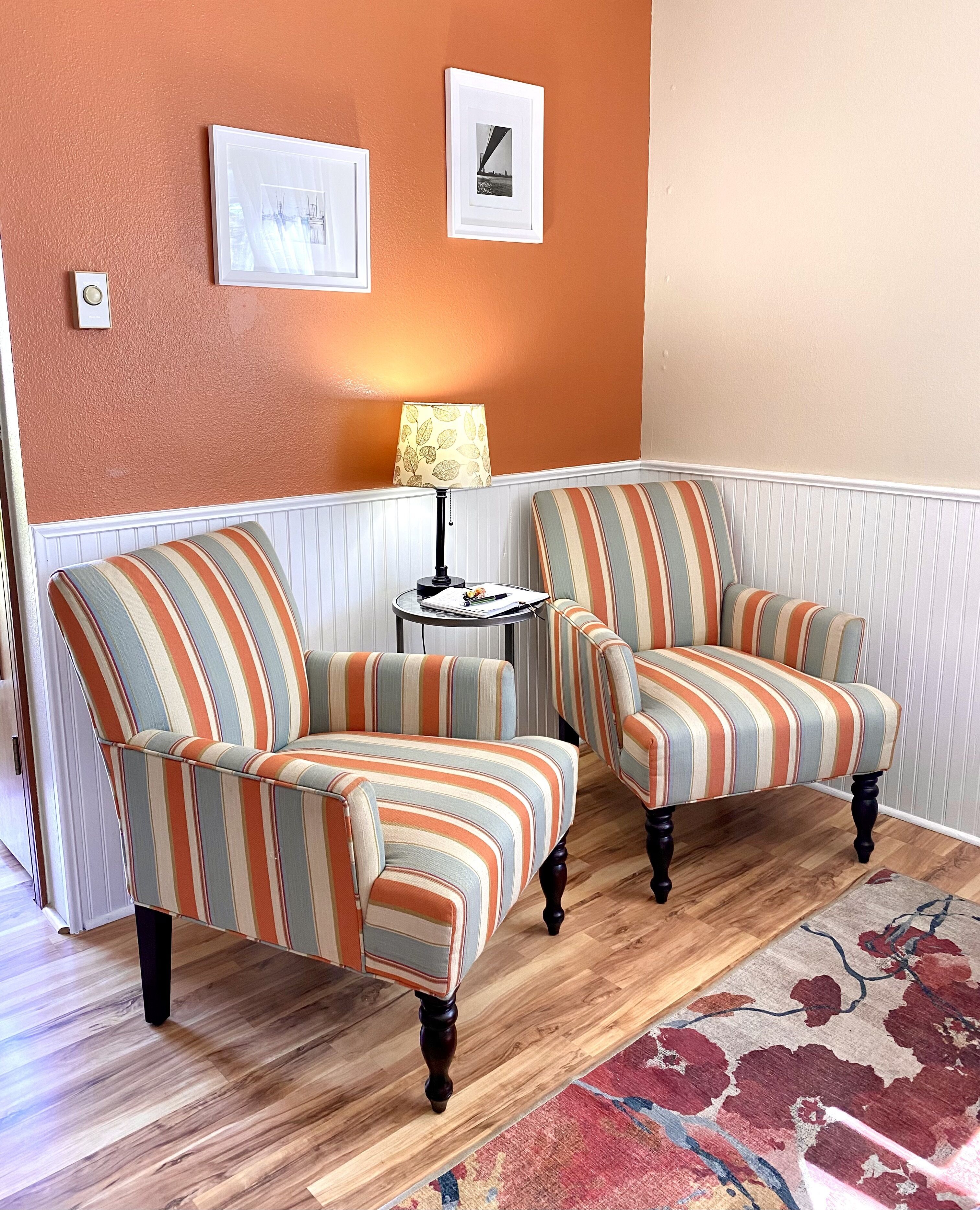 A room with two striped armchairs, a small round table with a lamp, and a patterned rug.