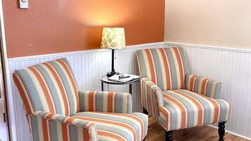 A room with two striped armchairs, a small round table with a lamp, and a patterned rug.