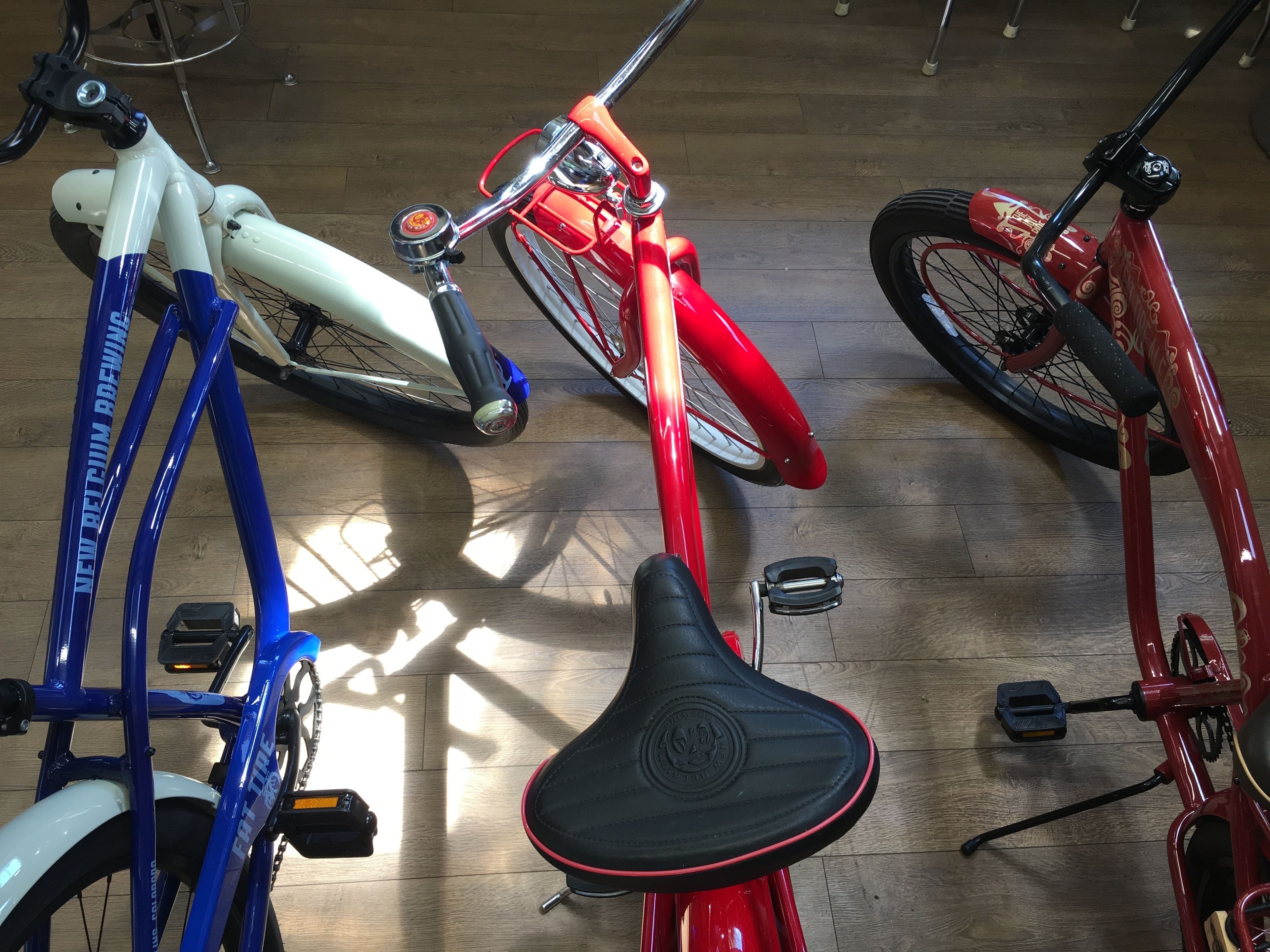 Drie fietsen met verschillende kleuren en designs, op een houten vloer geplaatst.