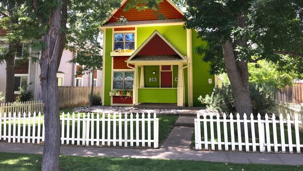 A two-story house with a green exterior, a red roof, and a white picket fence. - Remington Flats Hotel (Fort Collins)