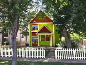 Una casa de dos pisos con fachada verde, tejado rojo y cerca de piquetes blancos.