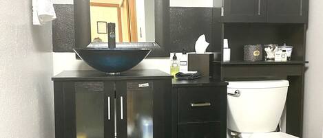 A bathroom with a black vanity, a large mirror, a white toilet, and a gray rug.