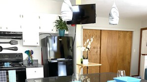 A modern kitchen with a central island, bar stools, a flat-screen TV, and a wooden cabinet. - Remington Flats Hotel (Fort Collins)