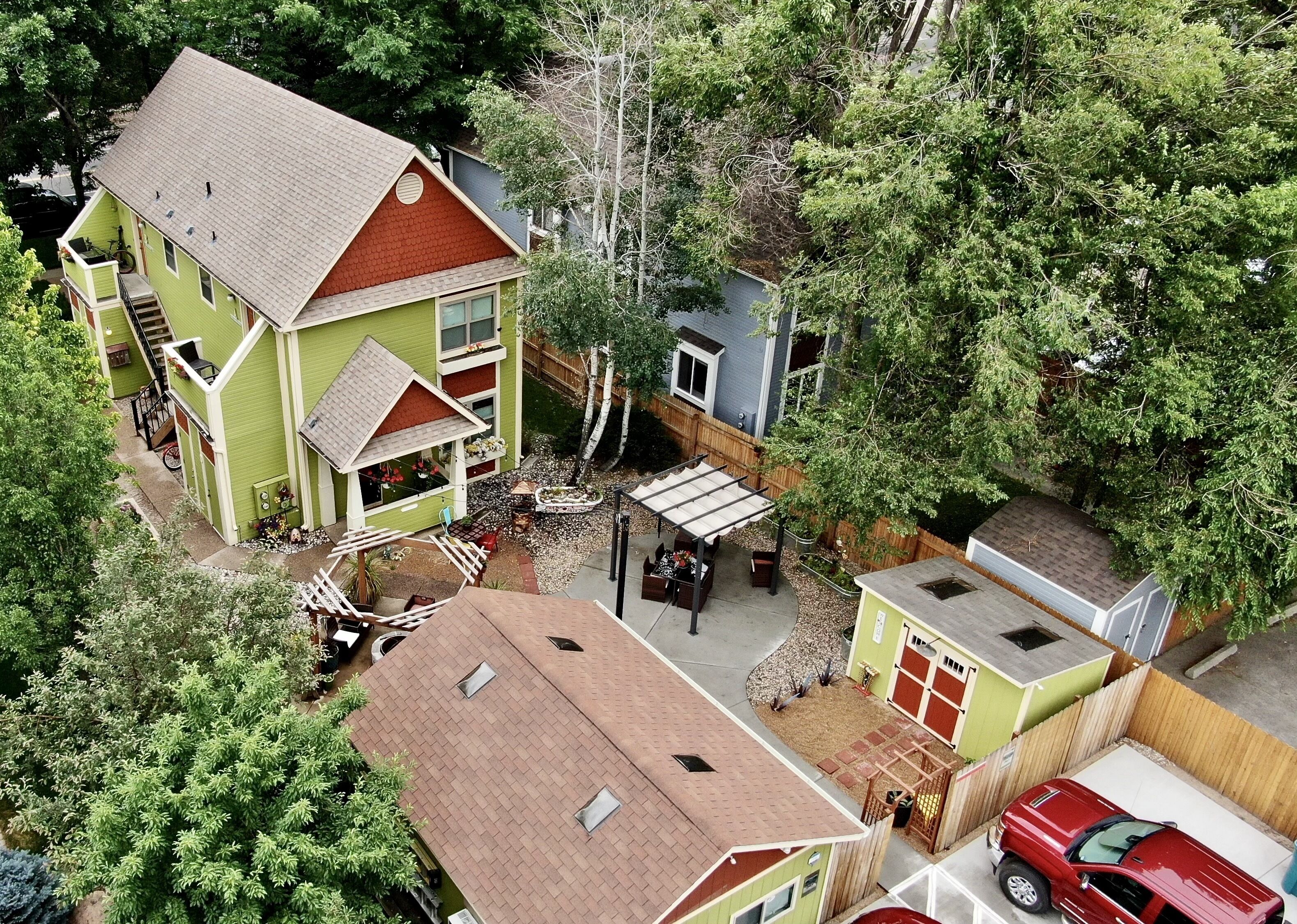 Une maison à deux étages, avec une façade verte, un toit rouge et une cour arrière clôturée.