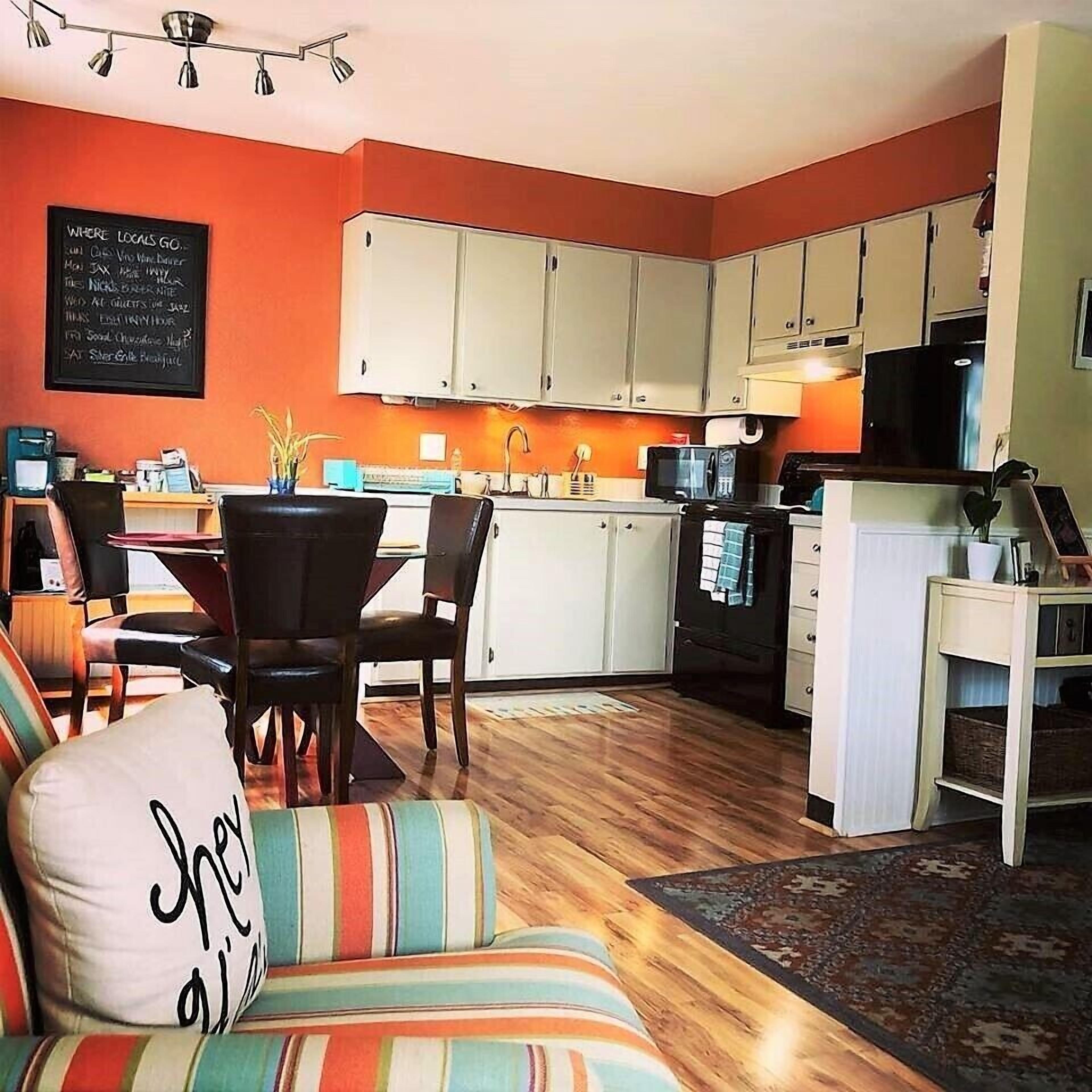 A cozy living room with a striped sofa, a dining area with a table and chairs, and a kitchen with white cabinets and appliances.