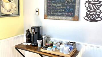 A coffee station with a chalkboard menu listing daily specials, a coffee machine, and various mugs and containers on a wooden table.