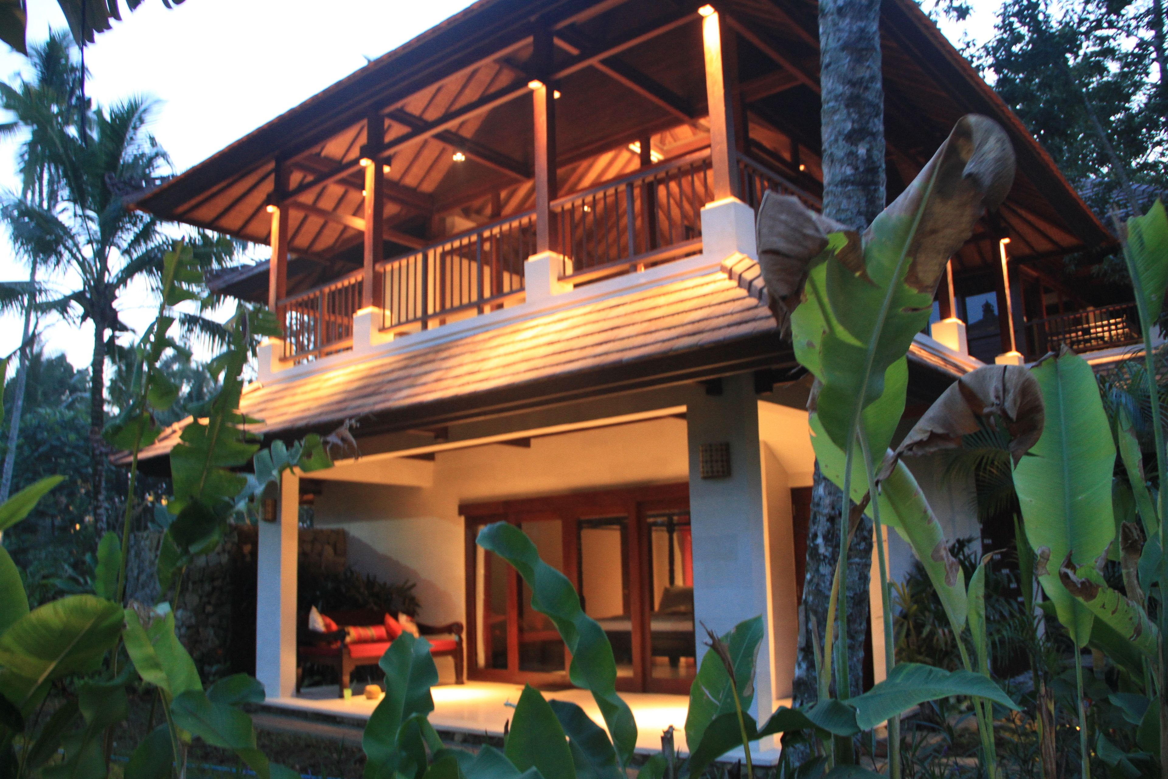 A two-story building with a balcony, surrounded by tropical vegetation.