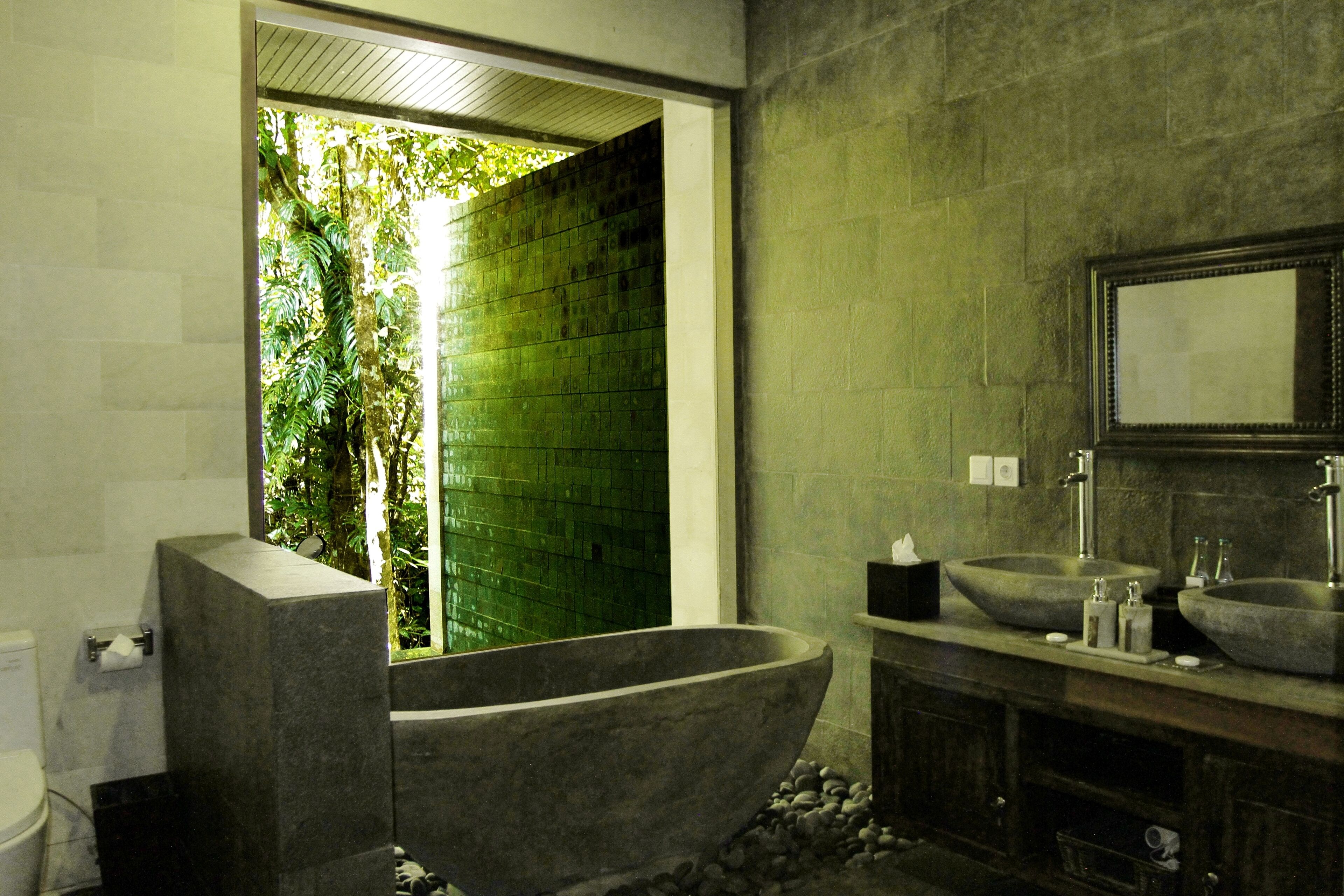 A bathroom with a freestanding bathtub, a large mirror, and a green-tiled wall.