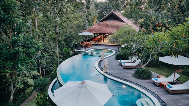 A pool with a wooden deck, lounge chairs, and umbrellas. - BeingSattvaa Luxury Ubud (Ubud)