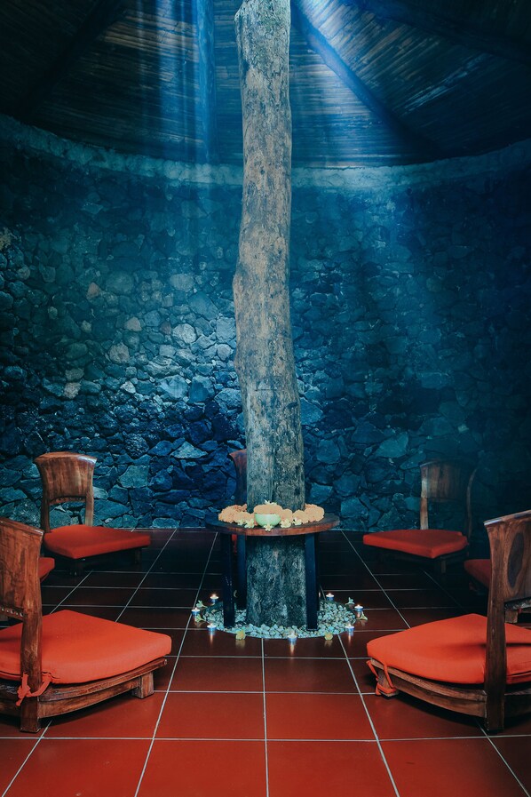 A stone-walled room with a wooden pillar, red cushioned chairs, and a small table with candles. - BeingSattvaa Luxury Ubud (Ubud)