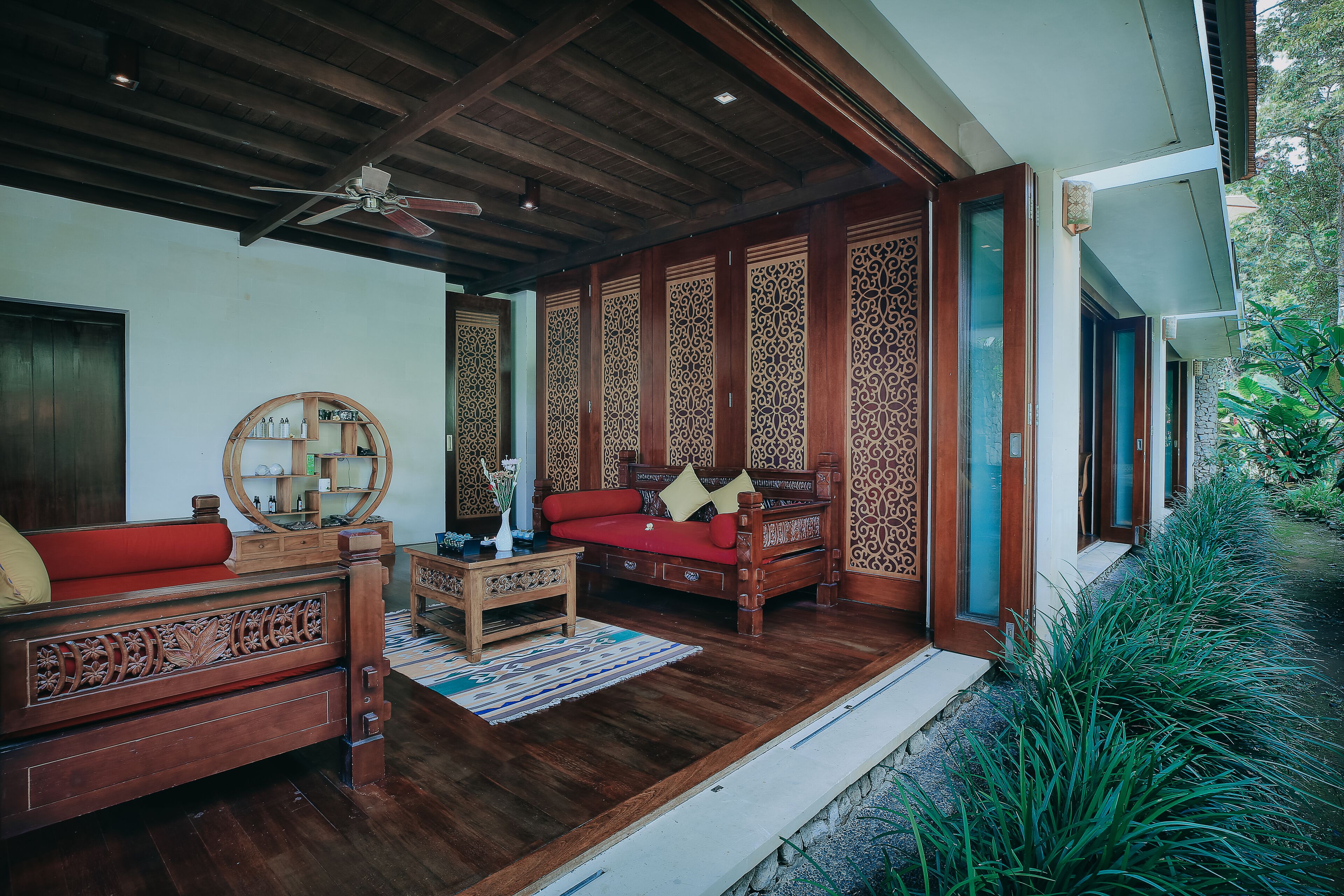 Un intérieur traditionnel en bois, avec un canapé rouge, une table basse en bois et un ventilateur de plafond.
