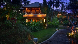 A resort with a wooden deck, lush tropical vegetation, and a well-lit building at dusk. - BeingSattvaa Luxury Ubud (Ubud)