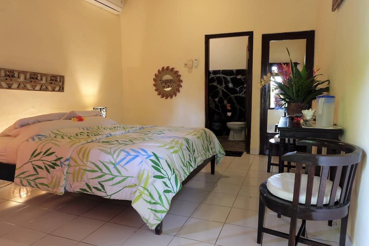 Une chambre à coucher avec un lit, une chaise, une petite table, un miroir et une plante en pot.