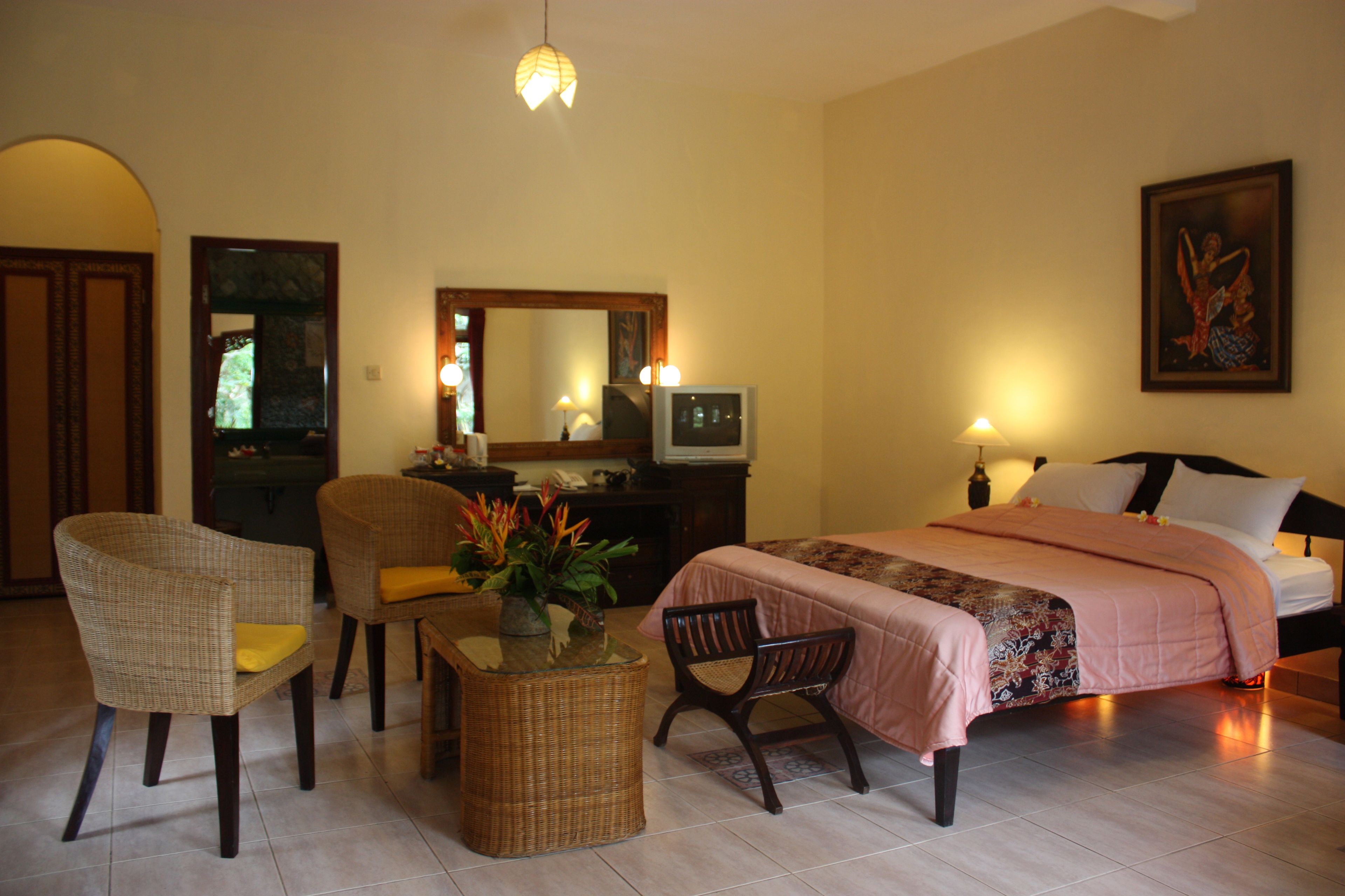 A bedroom with a bed, two chairs, a desk with a lamp, a television, and a mirror.
