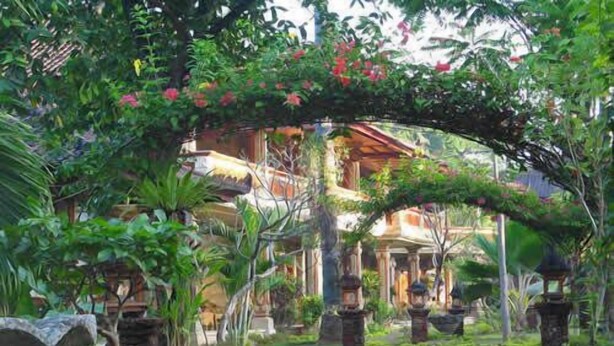 Un sendero conduce a un edificio tradicional con vestíbulo cubierto, rodeado de abundante vegetación y faroles de piedra.