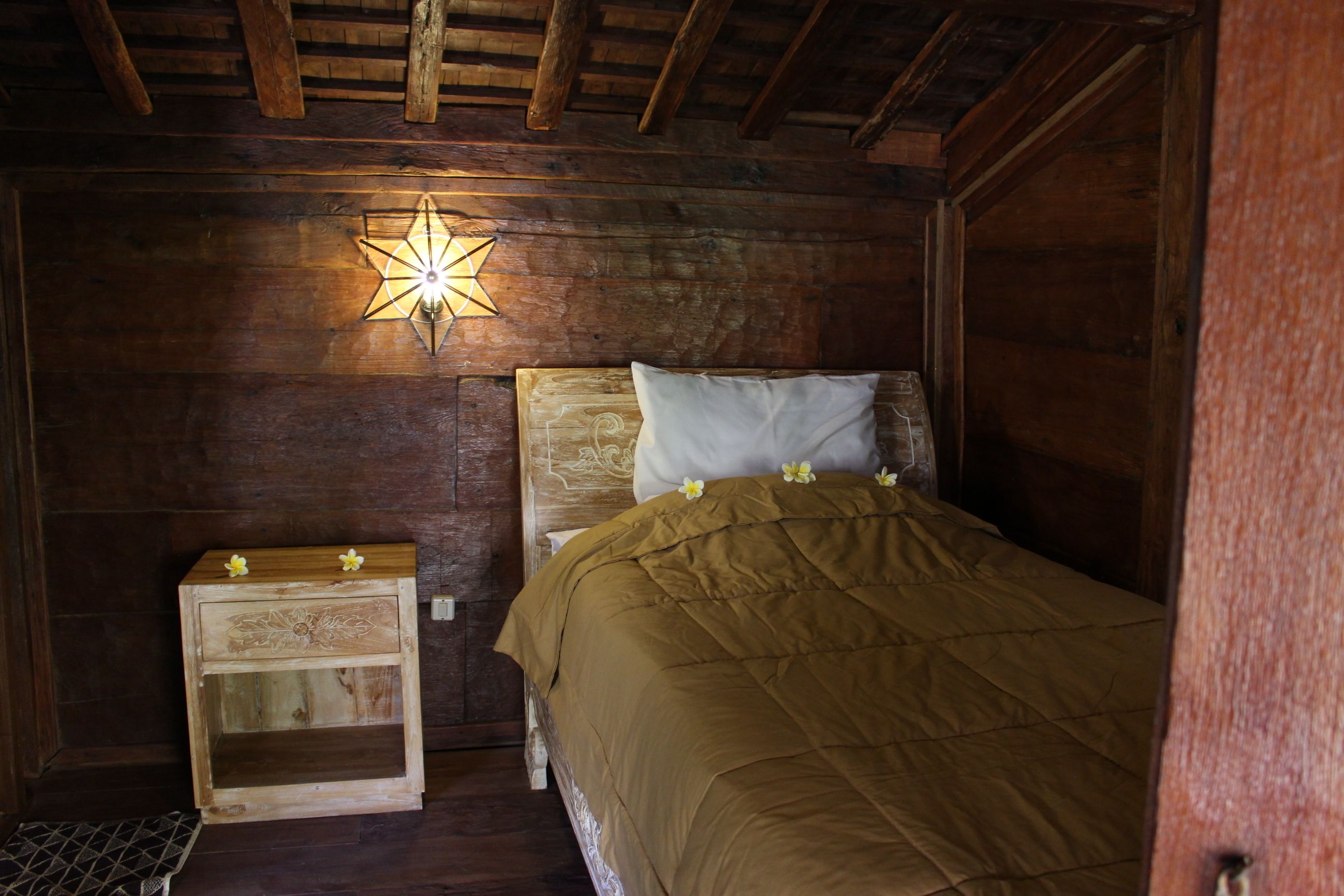 Habitación de cabaña de madera con una cama, una mesita de noche y una lámpara de pared con forma de estrella.