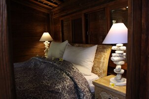 A wooden bedroom with a bed, two bedside lamps, and a decorative stack of stones.