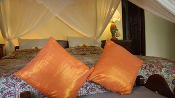 A bed with a canopy, two orange pillows, and a patterned bedspread.