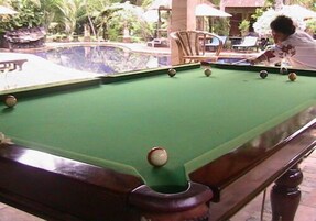 Una mesa de billar con bolas, rodeada de asientos exteriores y follaje.