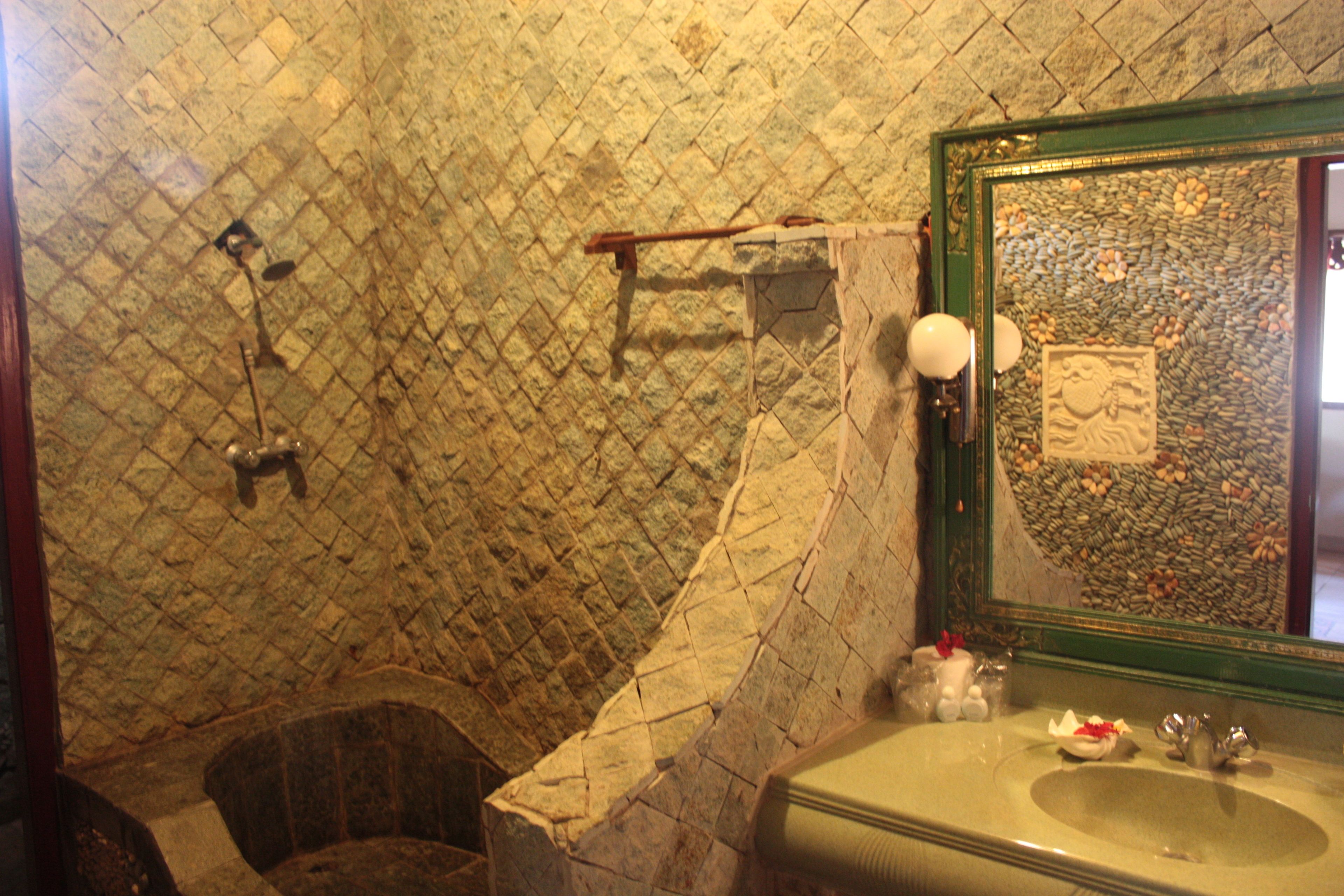 A bathroom with a stone wall, a wooden chair, a sink, and a mirror with a decorative frame.