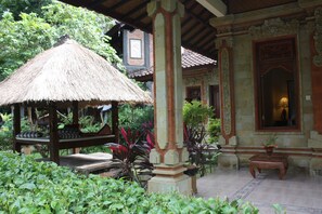 A traditional thatched-roof gazebo with a bench, surrounded by lush greenery.