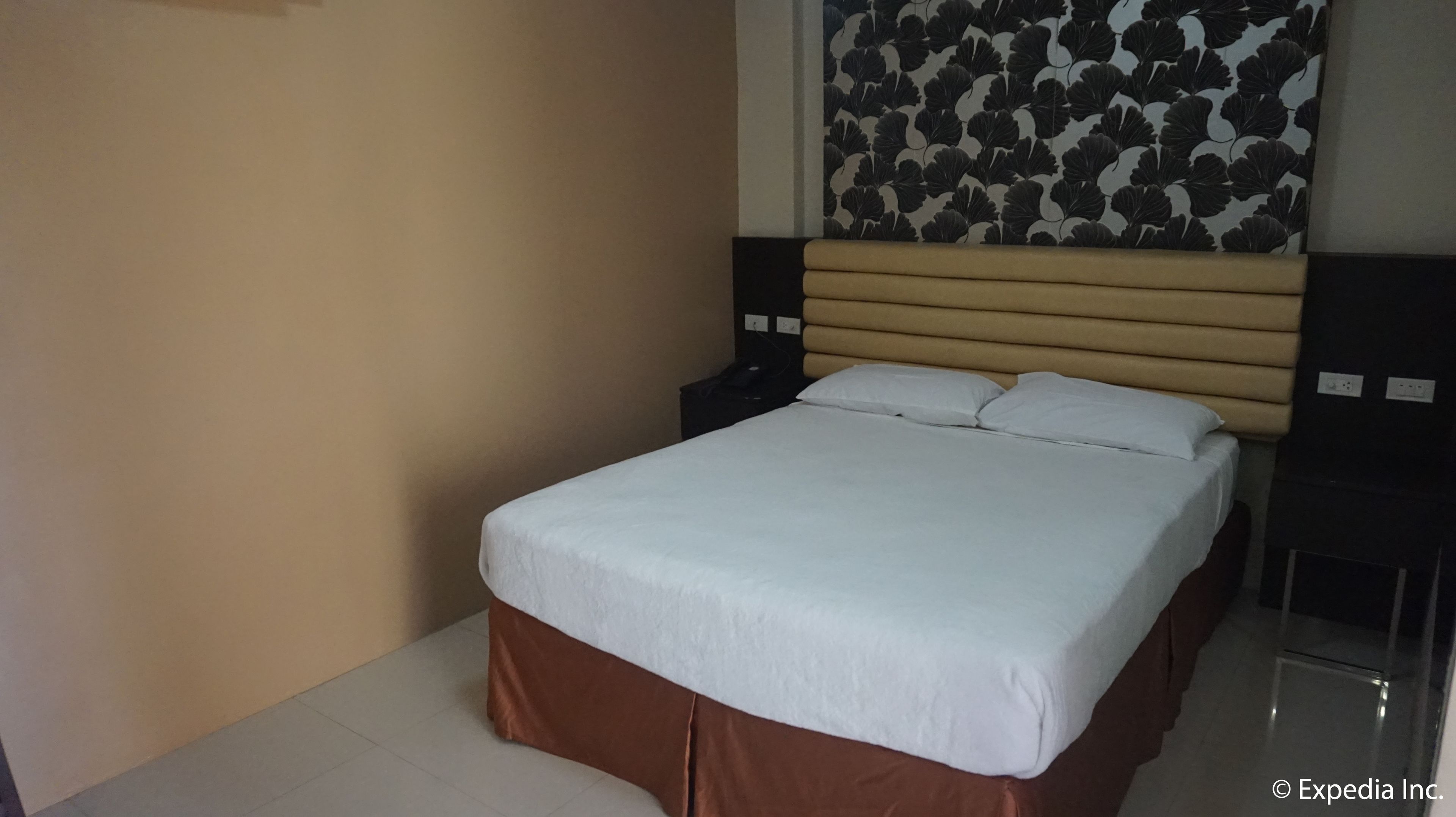 Een keurig opgemaakt bed met witte lakens, een houten hoofdbord en een muur met een bladmotief.
