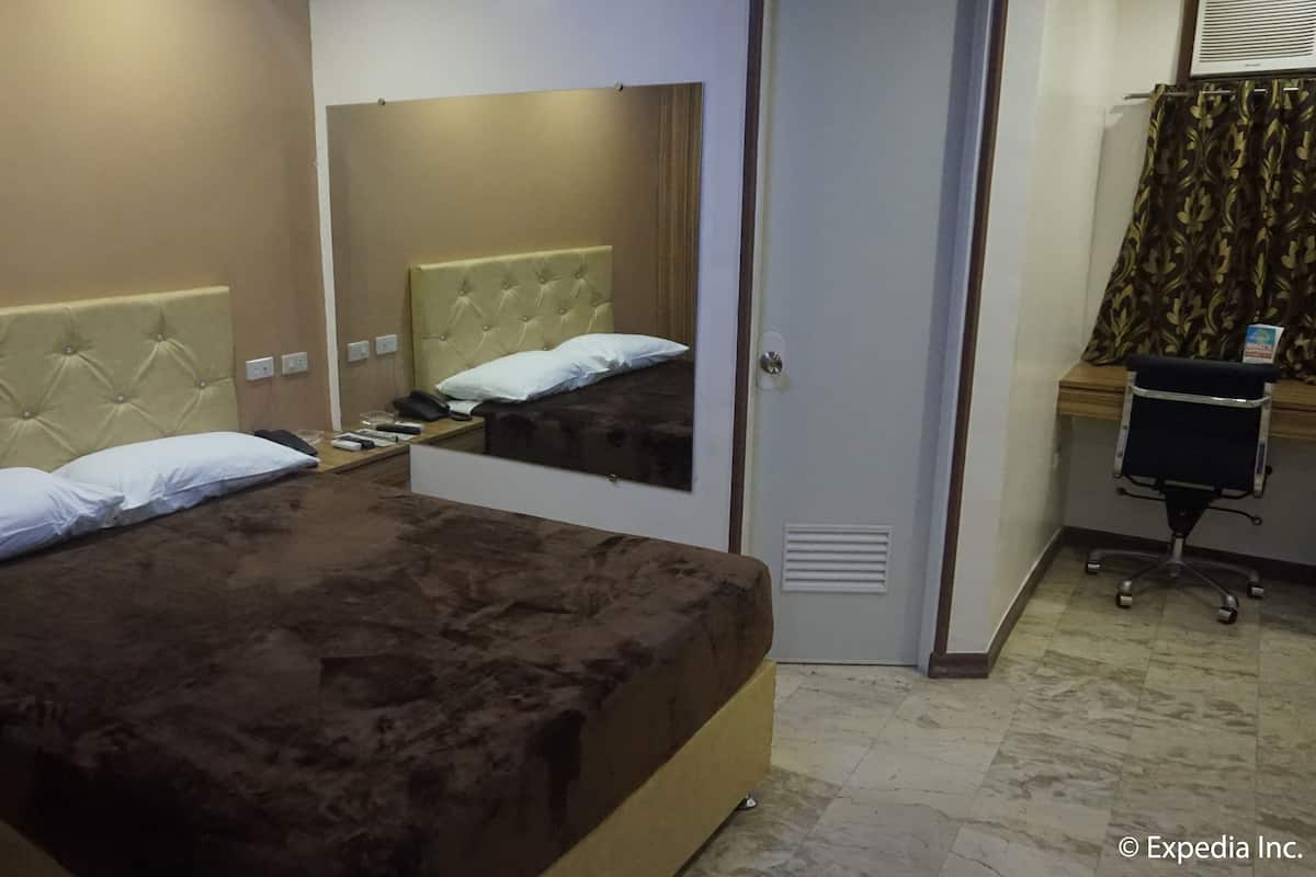 Habitación de hotel con una cama grande, una mesita de noche con teléfono y lámpara, un espejo, una puerta y un escritorio pequeño con una silla.