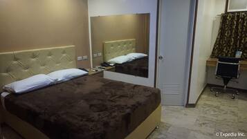 Habitación de hotel con una cama grande, una mesita de noche con teléfono y lámpara, un espejo, una puerta y un escritorio pequeño con una silla.