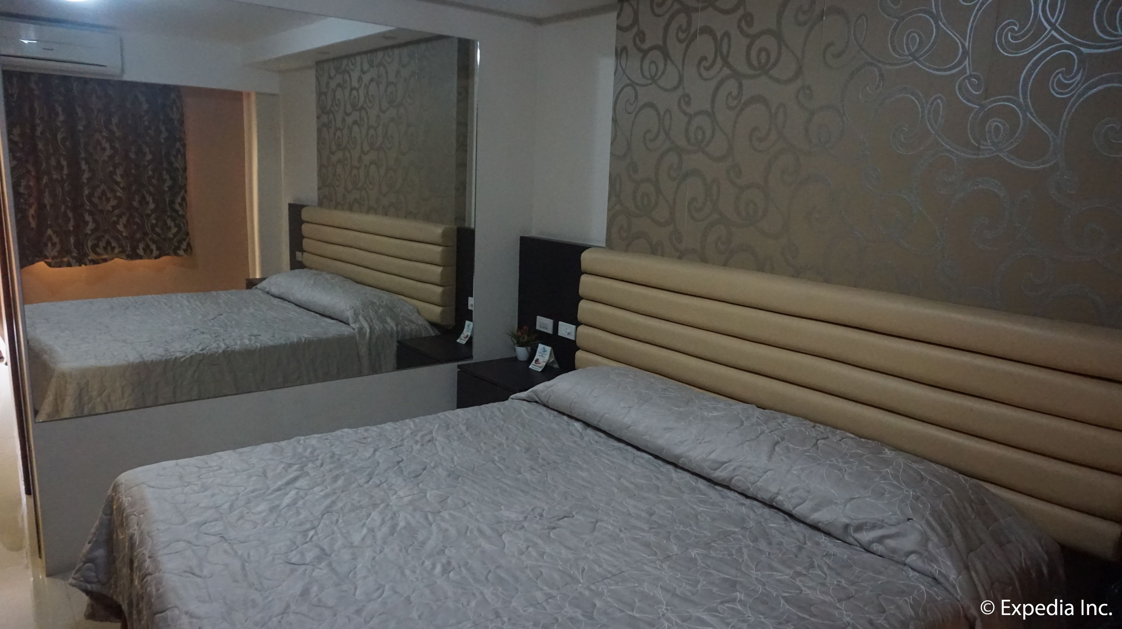 Una habitación de hotel con dos camas, un espejo, una mesita de noche y un papel tapiz estampado.
