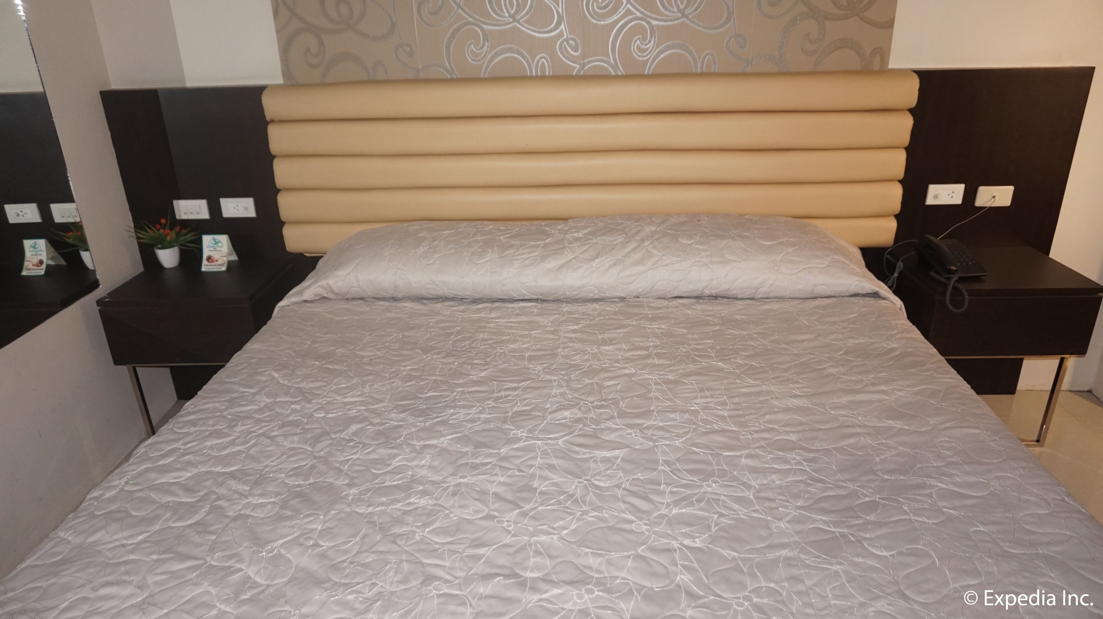 Ein Hotelzimmer mit einem großen Bett, einer Kopfteil, einem Nachttisch mit Telefon und einem kleinen Tisch mit Pflanze.
