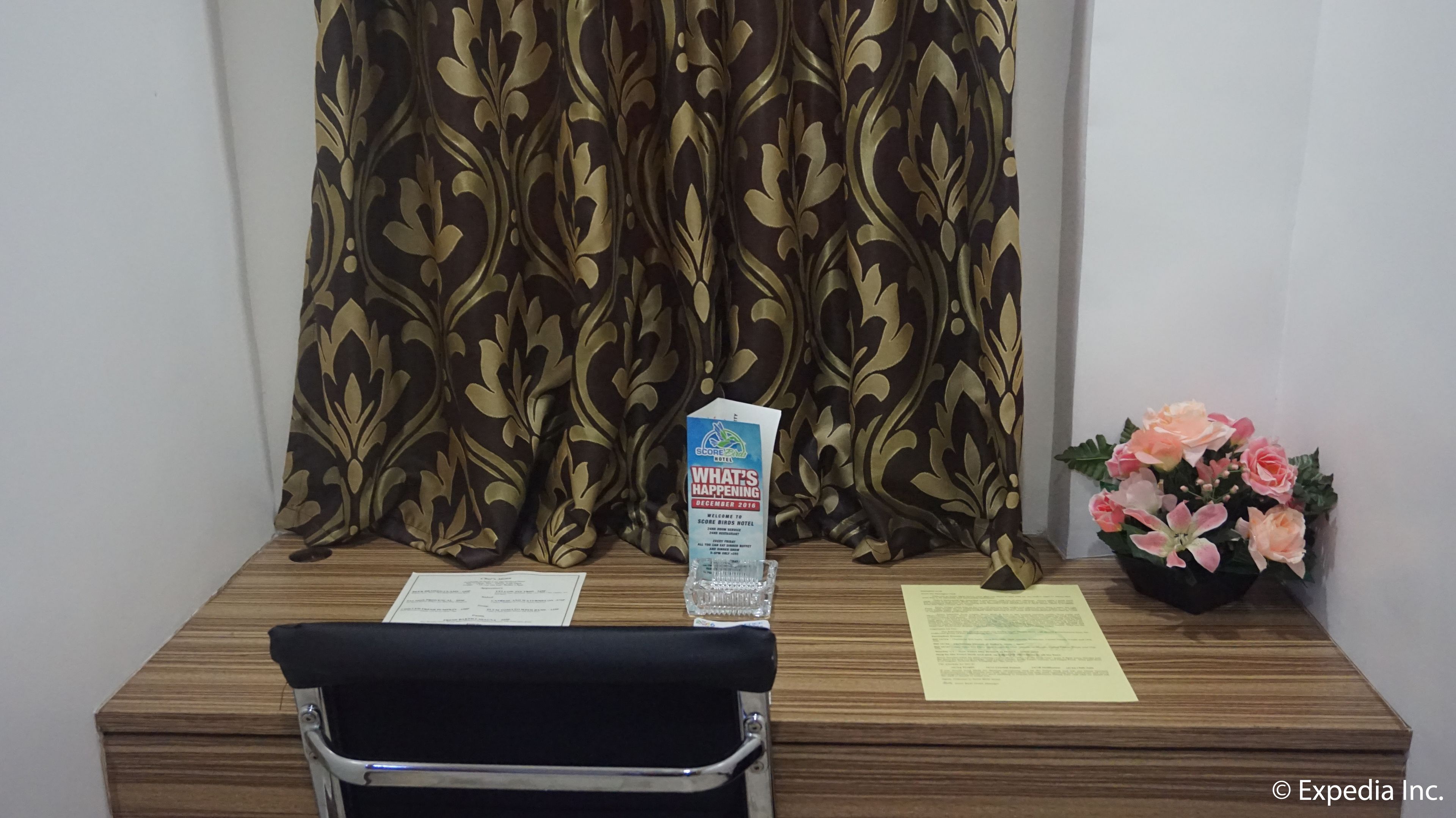 A wooden desk with a black chair, a water bottle, a welcome brochure, and a small flower arrangement.