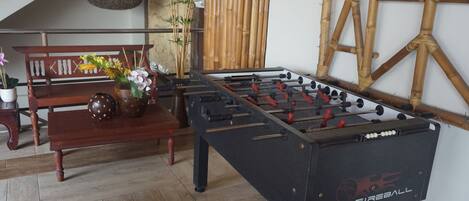 A Foosball table in a room with a wooden bench, a vase with flowers, and a bamboo wall decoration.