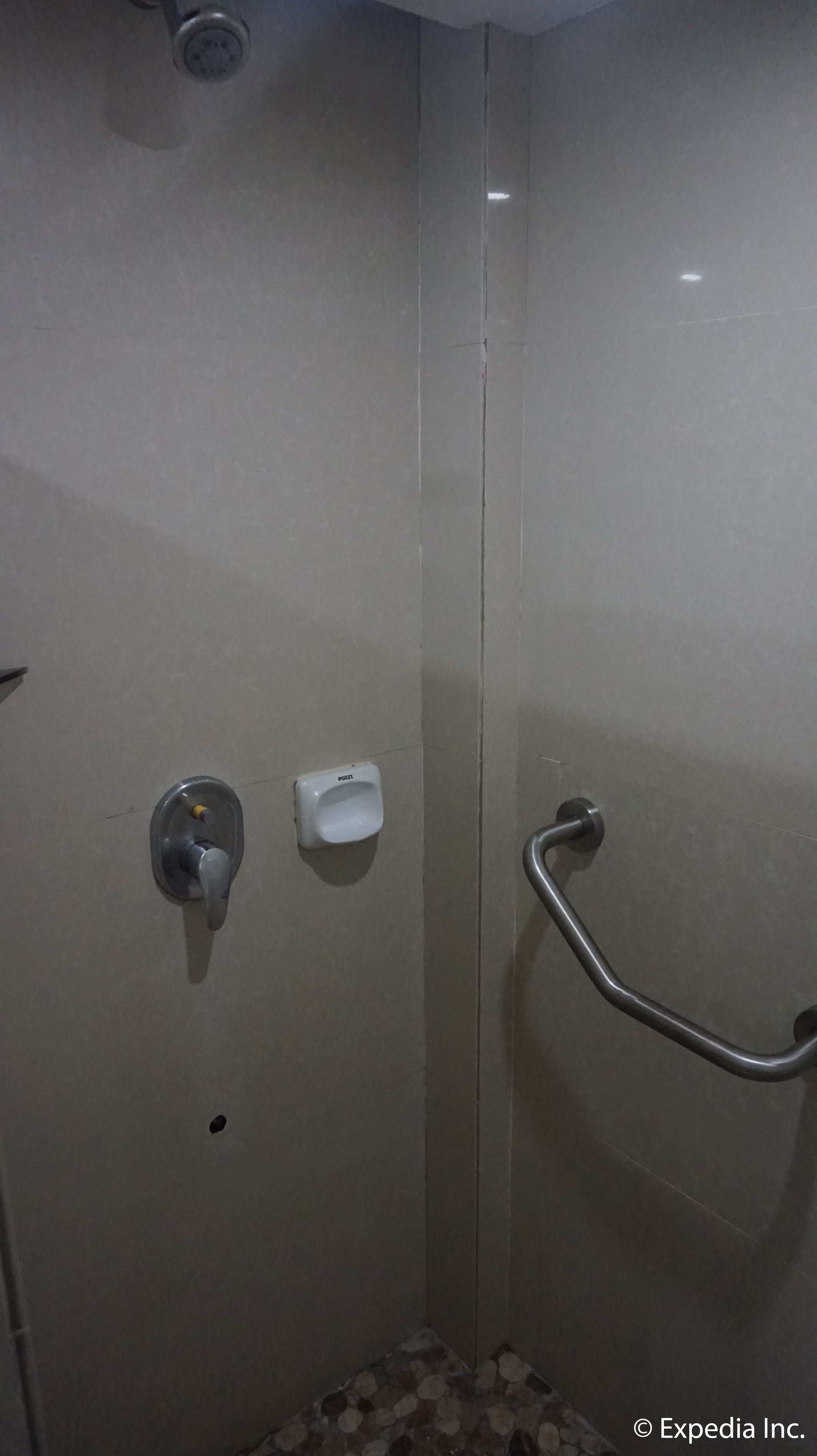 A shower stall with a handrail, a soap dispenser, and a faucet.