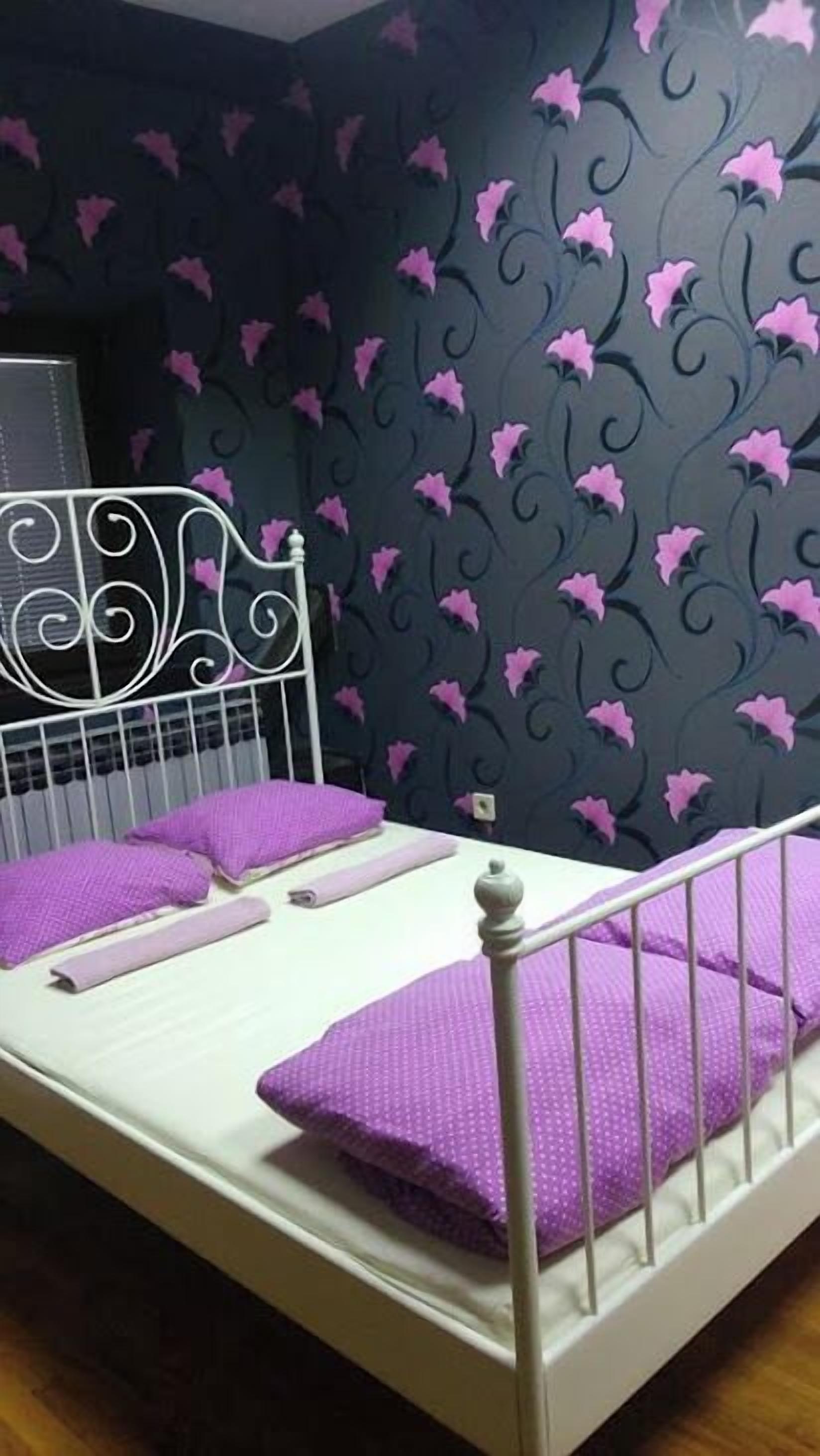 Una cama con estructura metálica, ropa de cama blanca y almohadas moradas.