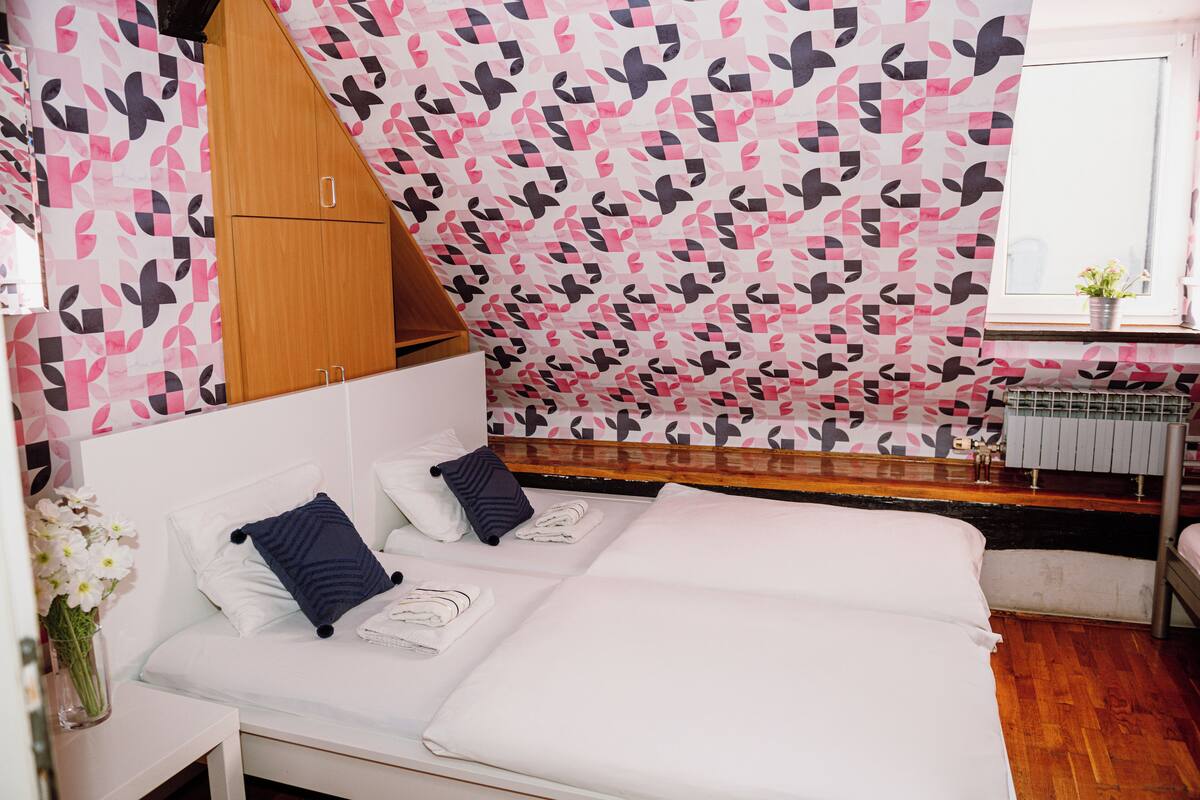 Ein Schlafzimmer mit Bett, Kissen, einem Holzschrank, einem Heizkörper und einem Fenster mit Pflanze.