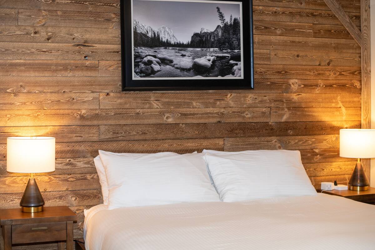 A bedroom with a wooden wall, a framed photograph of a river, and two bedside lamps.