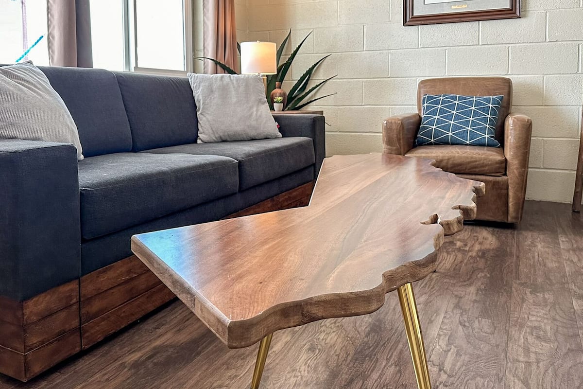A living room with a dark blue sofa, a wooden coffee table with gold legs, and a brown armchair with a patterned cushion.