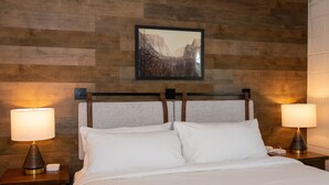 A hotel room with a wooden headboard, two bedside lamps, a framed picture on the wall, and a neatly made bed with white linens. - Gull Lake Lodge (June Lake)