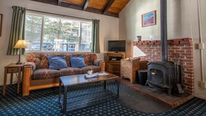 A cozy living room with a wooden ceiling, a brick fireplace, a television, and a patterned sofa. - Gull Lake Lodge (June Lake)