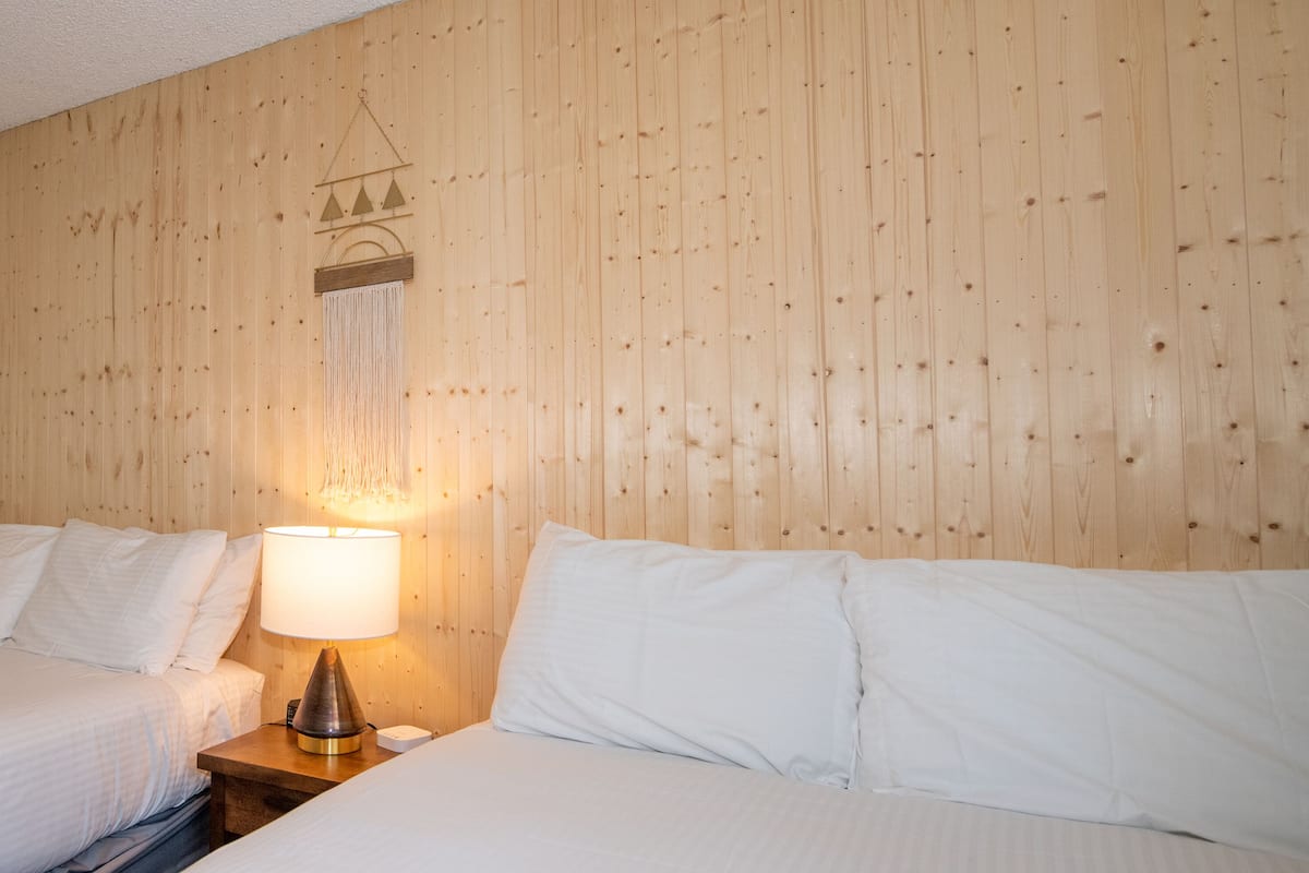 A hotel room with two beds, a wooden headboard, a hanging light fixture, and a small bedside table.