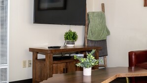 A living room with a wooden TV stand, a small potted plant, a remote control, and a green towel hanging on a wooden chair. - Gull Lake Lodge (June Lake)