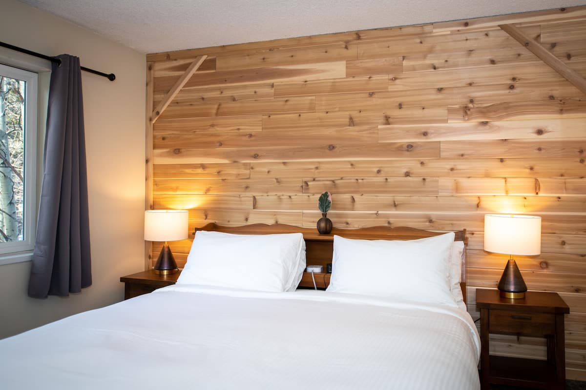 A neatly made bed with white linens, two bedside lamps, and a wooden headboard.