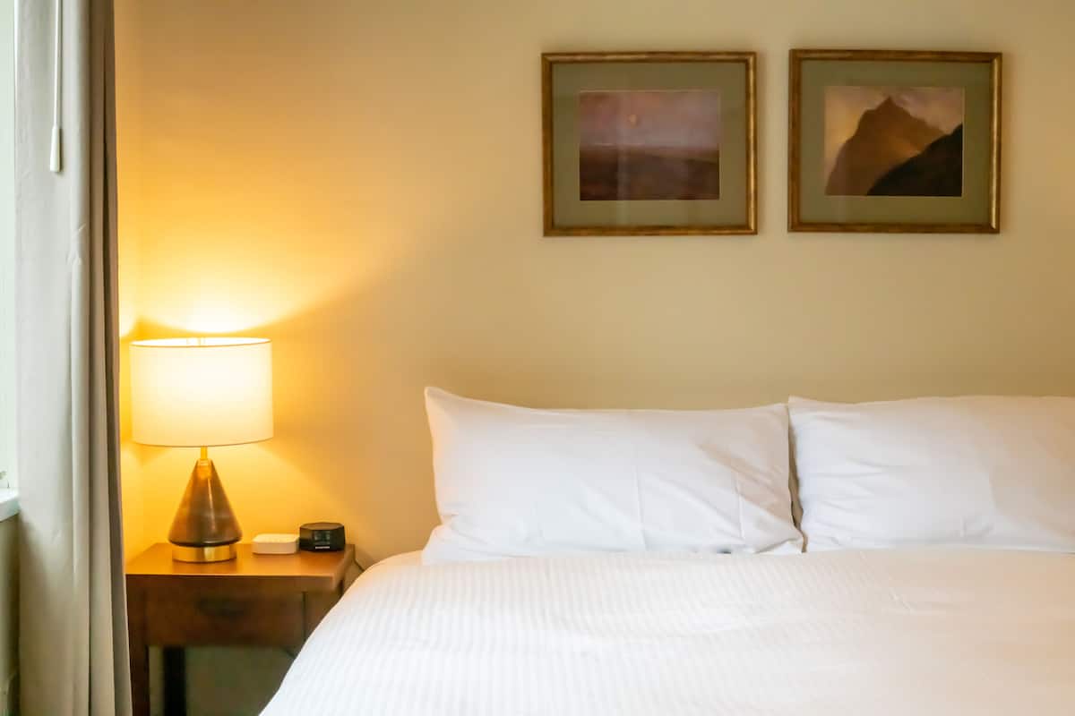 A hotel room with a bed, a nightstand with a lamp, and two framed pictures on the wall.