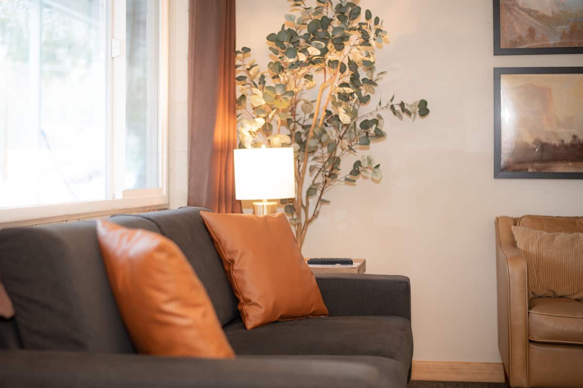 A living room with a sofa, a side table, a lamp, a plant, and a chair.