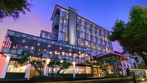 Un hotel moderno con fachada de vidrio, varios pisos y una entrada bien iluminada.